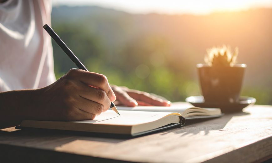 Persona escribiendo un relato de escritura de ficción en un cuaderno.